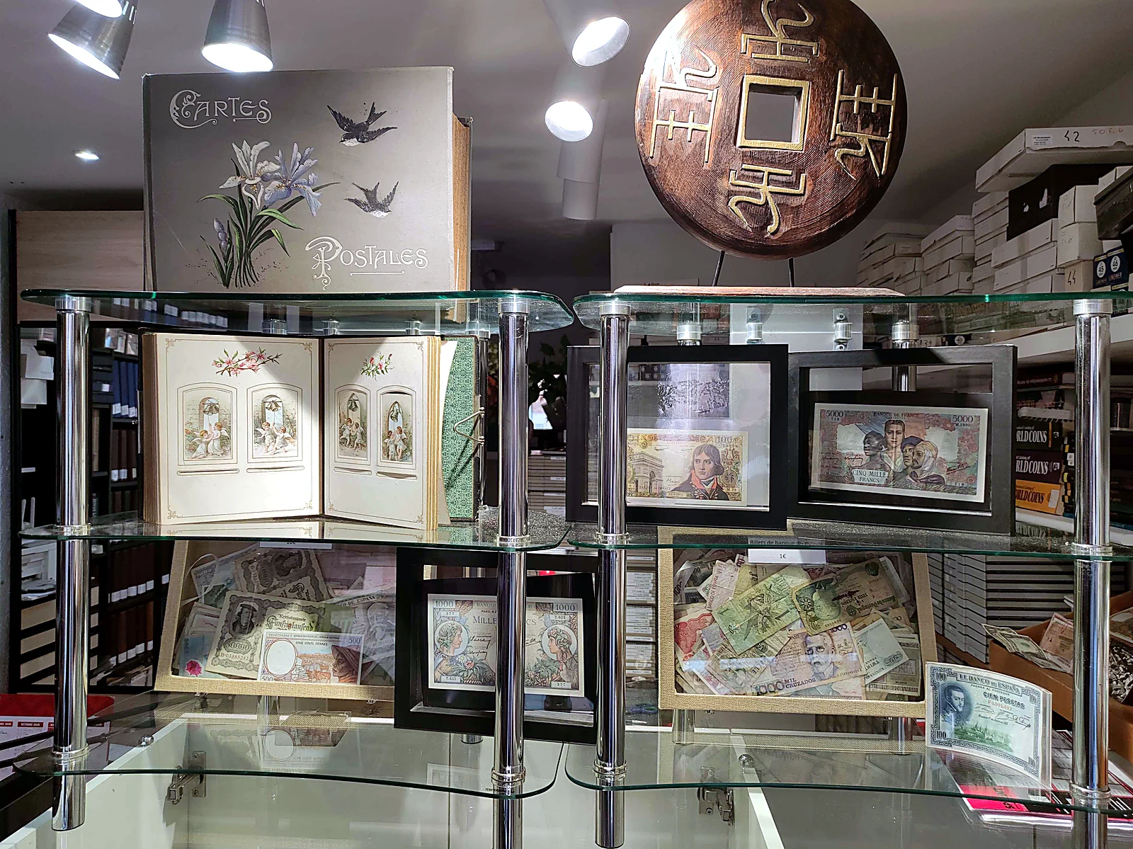 Vitrines en verre : album de cartes postales Art nouveau, grande sapèque chinoise et billets encadrés